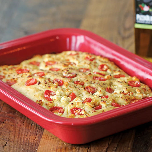 Baked dish with tomatoes in a red rectangular baking tray on a wooden surface